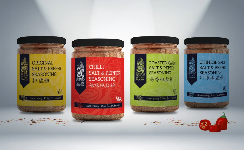 Four clear glass jars of Golden Dragon Salt and Pepper Seasoning—Original, Chilli, Roasted Garlic, and Chinese Spice—displayed in a row on a white surface with scattered spices and red chillies.
